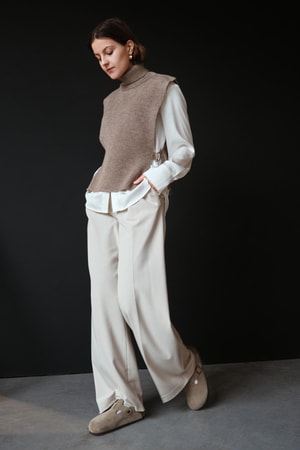 Kuvassa nainen, jolla yllään tumma greige neuleliivi muhkealla poolokauluksella.